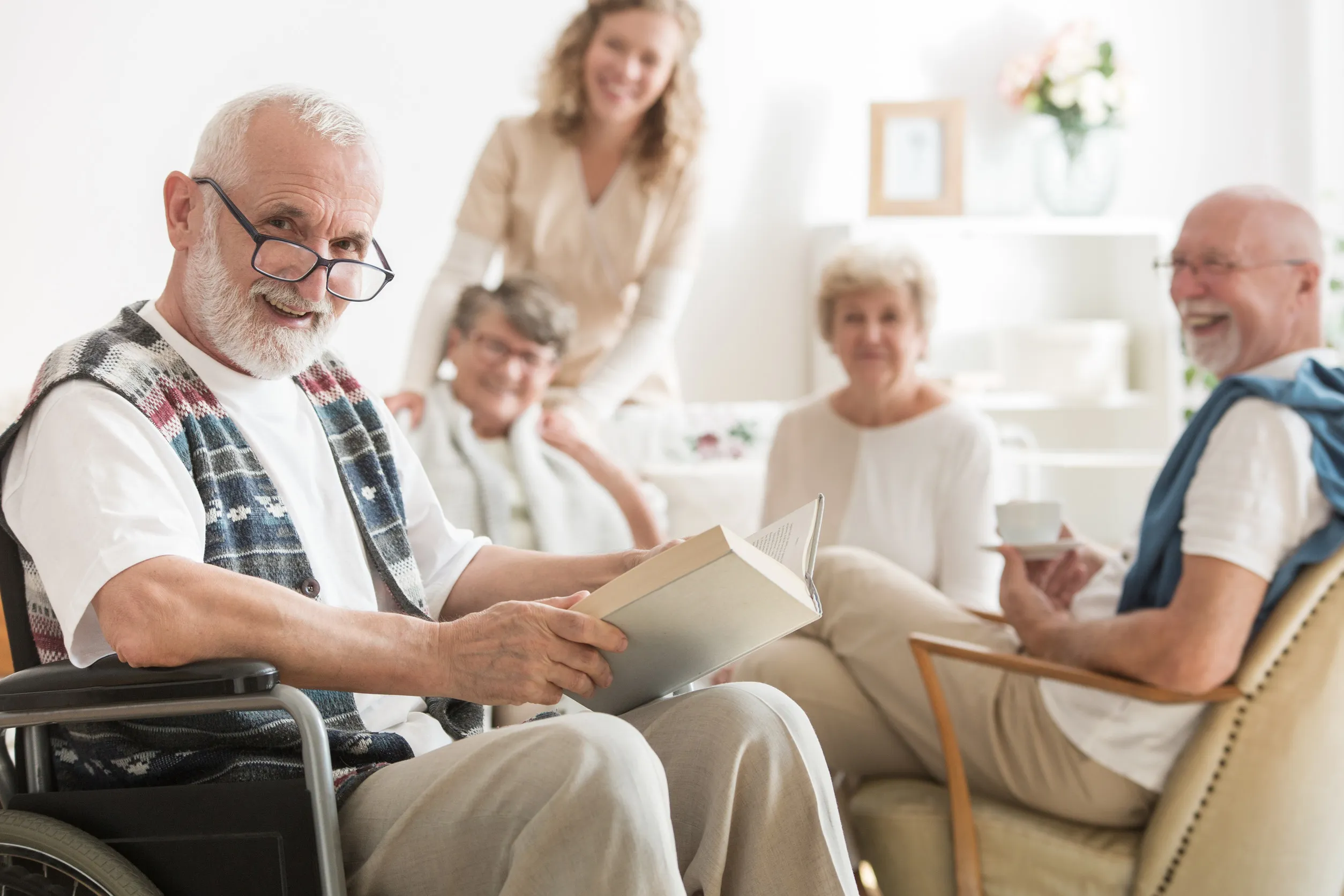 Old man with glasses sitting on wheelchair reading a book